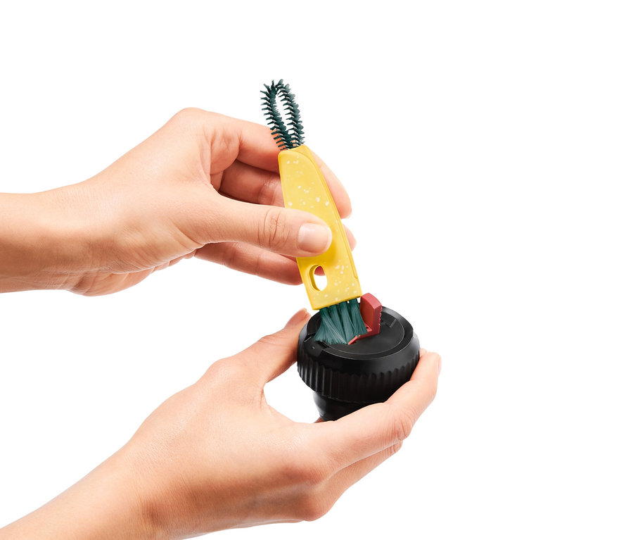 Des mains nettoient un appareil noir avec une brosse multifonction 3 en 1 jaune.