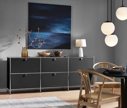 Buffet bas « CN3 » noir avec 6 abattants, lampe de table blanche avec abat-jour en tissu et lampes à suspension avec globes en verre.