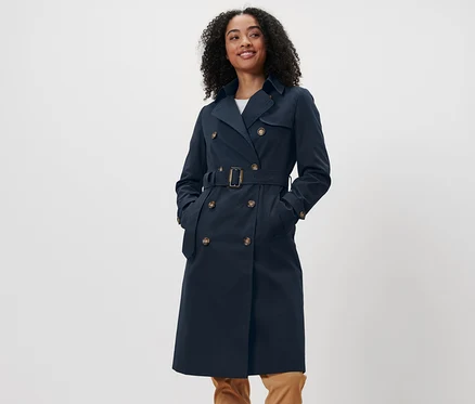 Une femme aux cheveux foncés se tient debout et porte un trench-coat bleu marine.