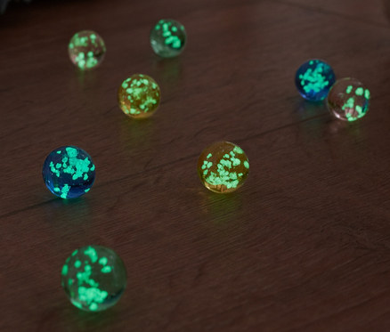 Des billes lumineuses sont posées sur un plancher en bois, à côté d'une couverture à franges et d'une peluche.