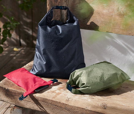 Trois sacs fourre-tout imperméables posés sur un banc en bois.
