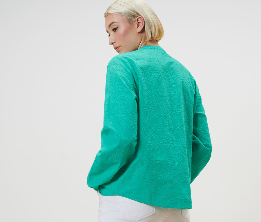 Femme posant dans un chemisier vert à broderie.