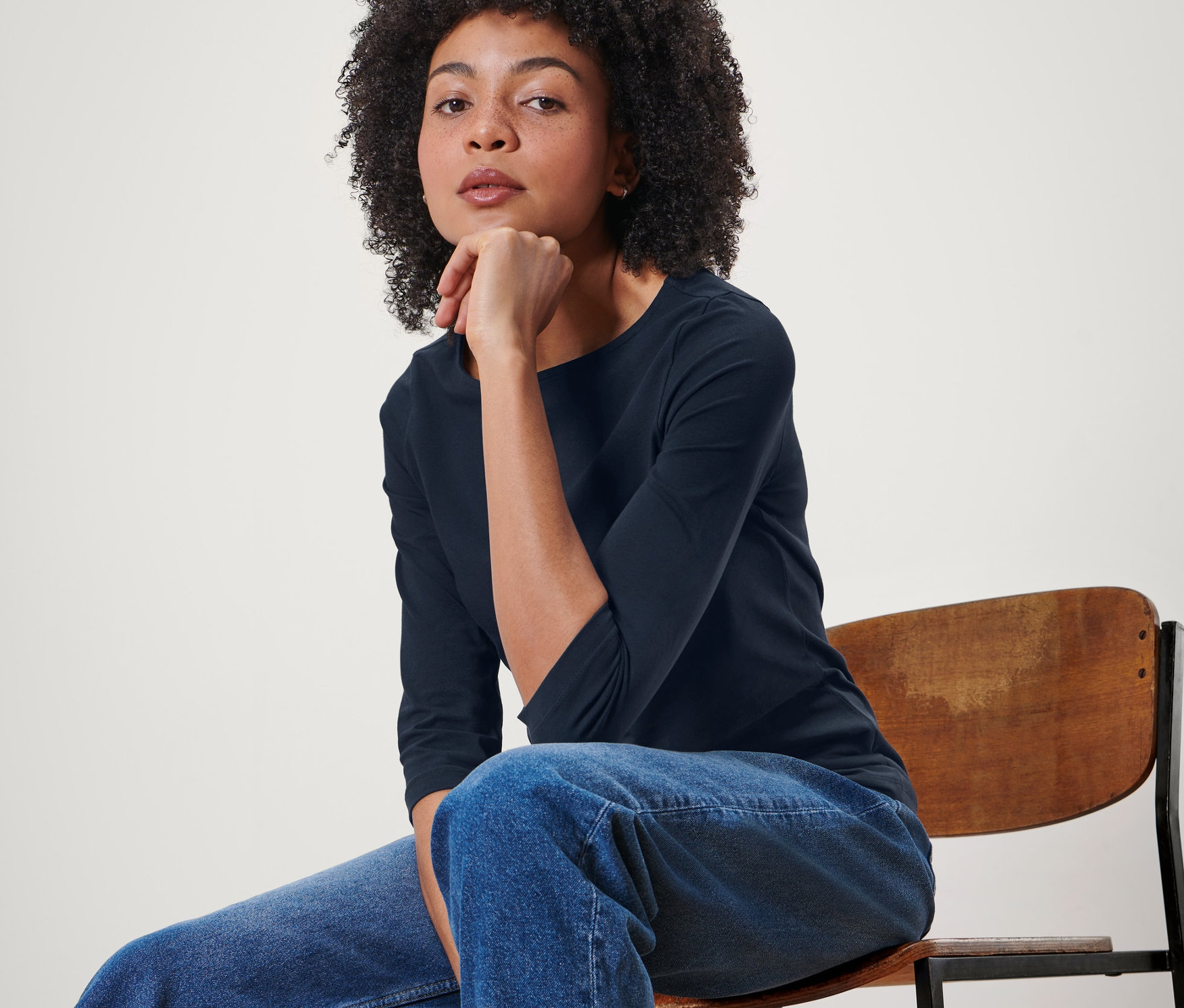 Femme assise sur une chaise portant un t-shirt bleu foncé à manches 3/4.