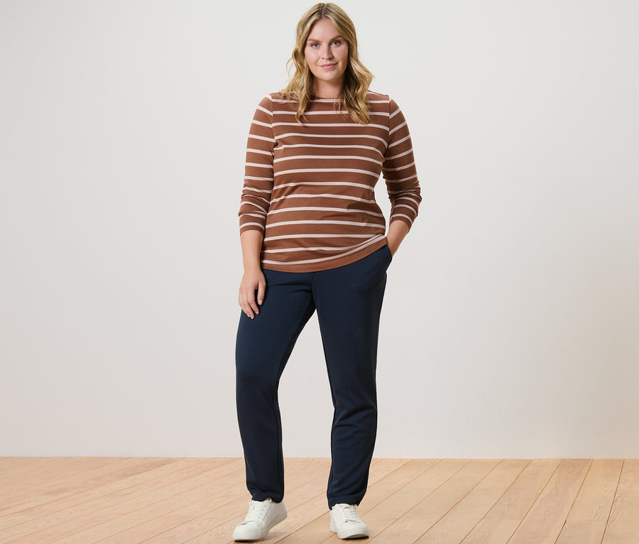 Femme posant en t-shirt rayé à manches longues cognac et pantalon de jogging.