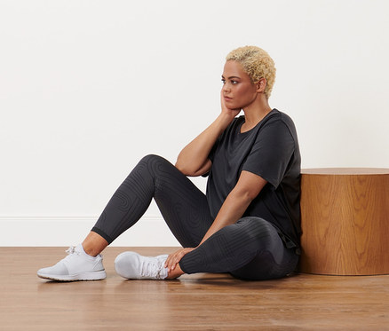 Femme assise par terre portant un t-shirt de sport anthracite et un legging de sport réversible noir.