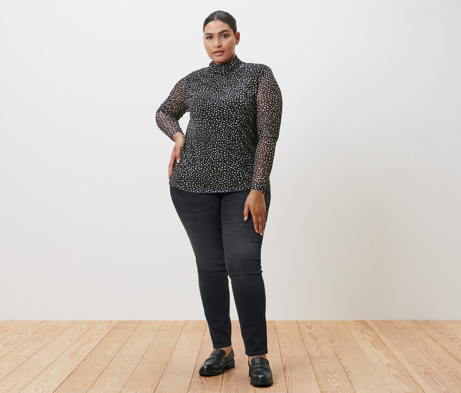 Femme posant dans une chemise à col roulé en mesh avec pois, un jean noir et des chaussures.