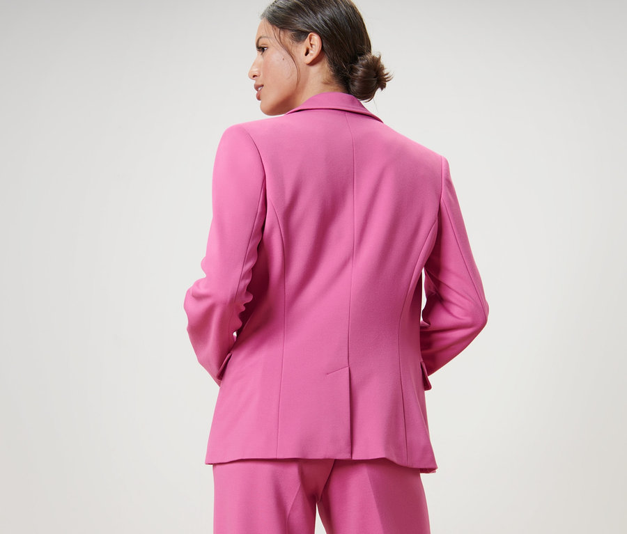 Femme portant un ensemble rose, comprenant un blazer en jersey.