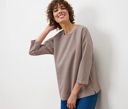 Une femme est appuyée contre un mur et porte un sweat-shirt à carreaux et un jean.