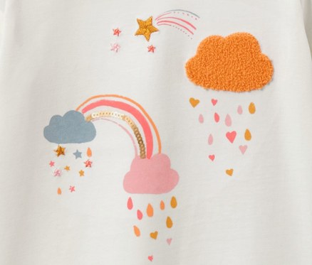 Détail d'un t-shirt blanc à manches longues pour enfant avec motif arc-en-ciel et nuages.