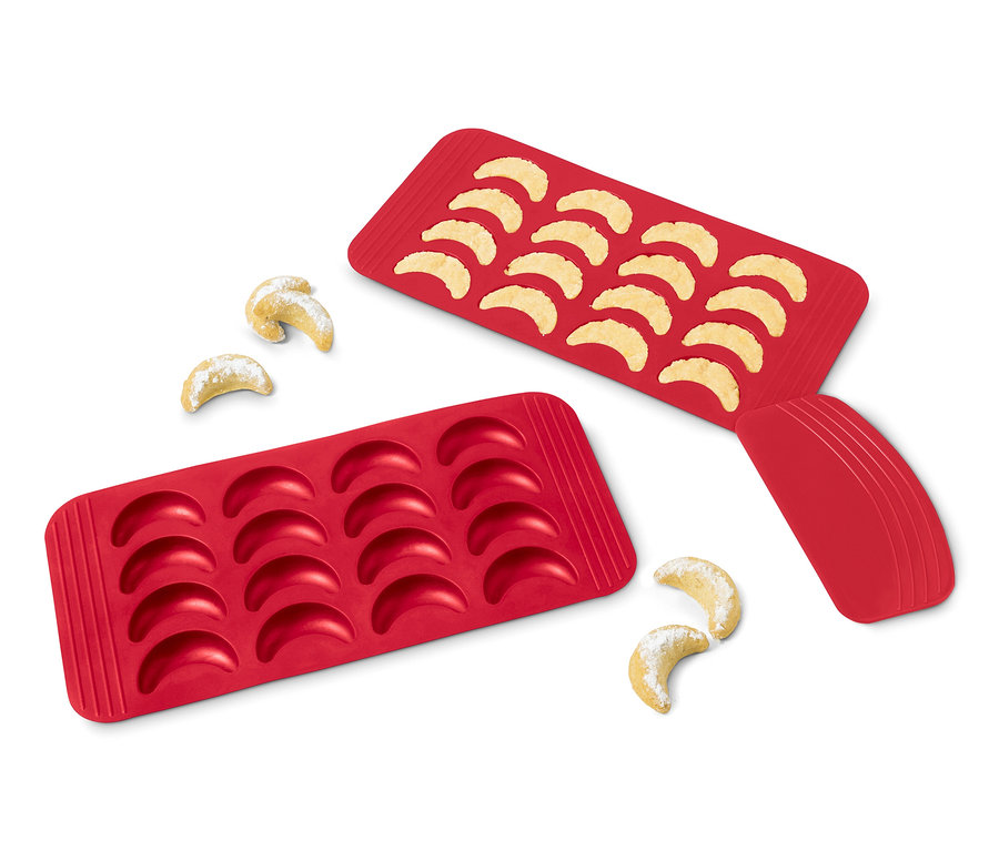 Deux tapis de cuisson rouges pour croissants vanillés, un rempli de croissants cuits, l'autre vide, et quelques croissants à côté.