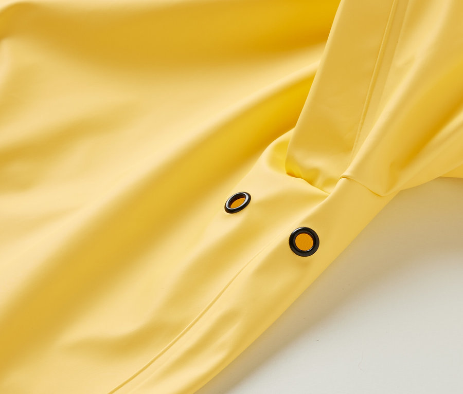 Détail d'un parka de pluie jaune « ciré » avec des œillets noirs.