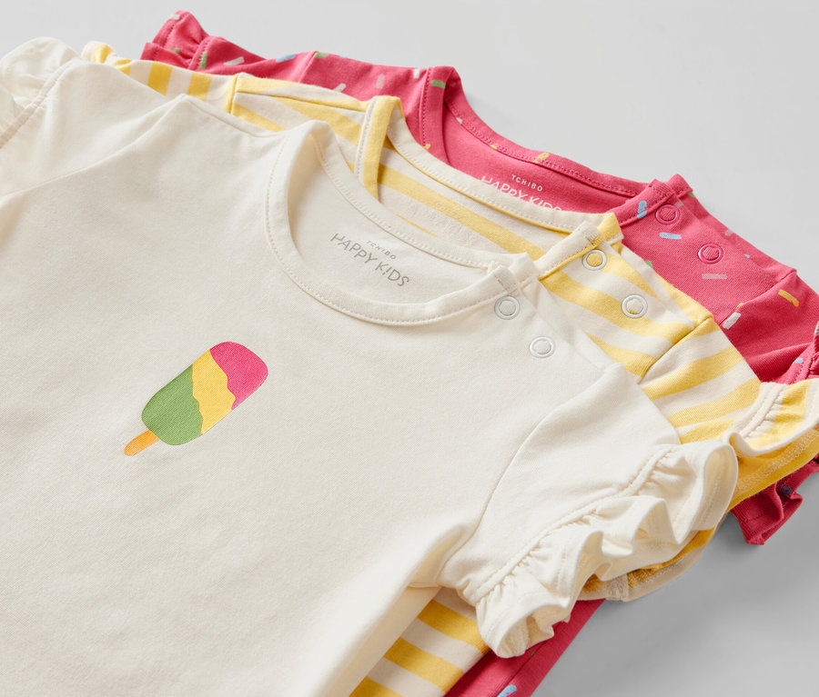 Trois t-shirts pour bébé : un couleur crème avec un motif de glace, un jaune rayé et un rose avec un imprimé.