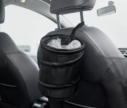Une poubelle pliable noire est accrochée à l'arrière d'un siège de voiture.