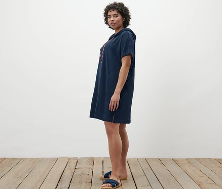Une femme debout de profil porte une robe de plage bleue en tissu éponge.