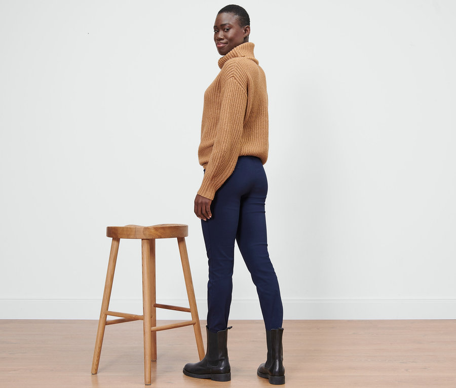 Une femme pose à côté d'un tabouret et porte un pantalon stretch bleu.
