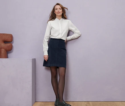 Femme posant en chemisier avec détails ruchés, jupe en velours côtelé et loafers en cuir.
