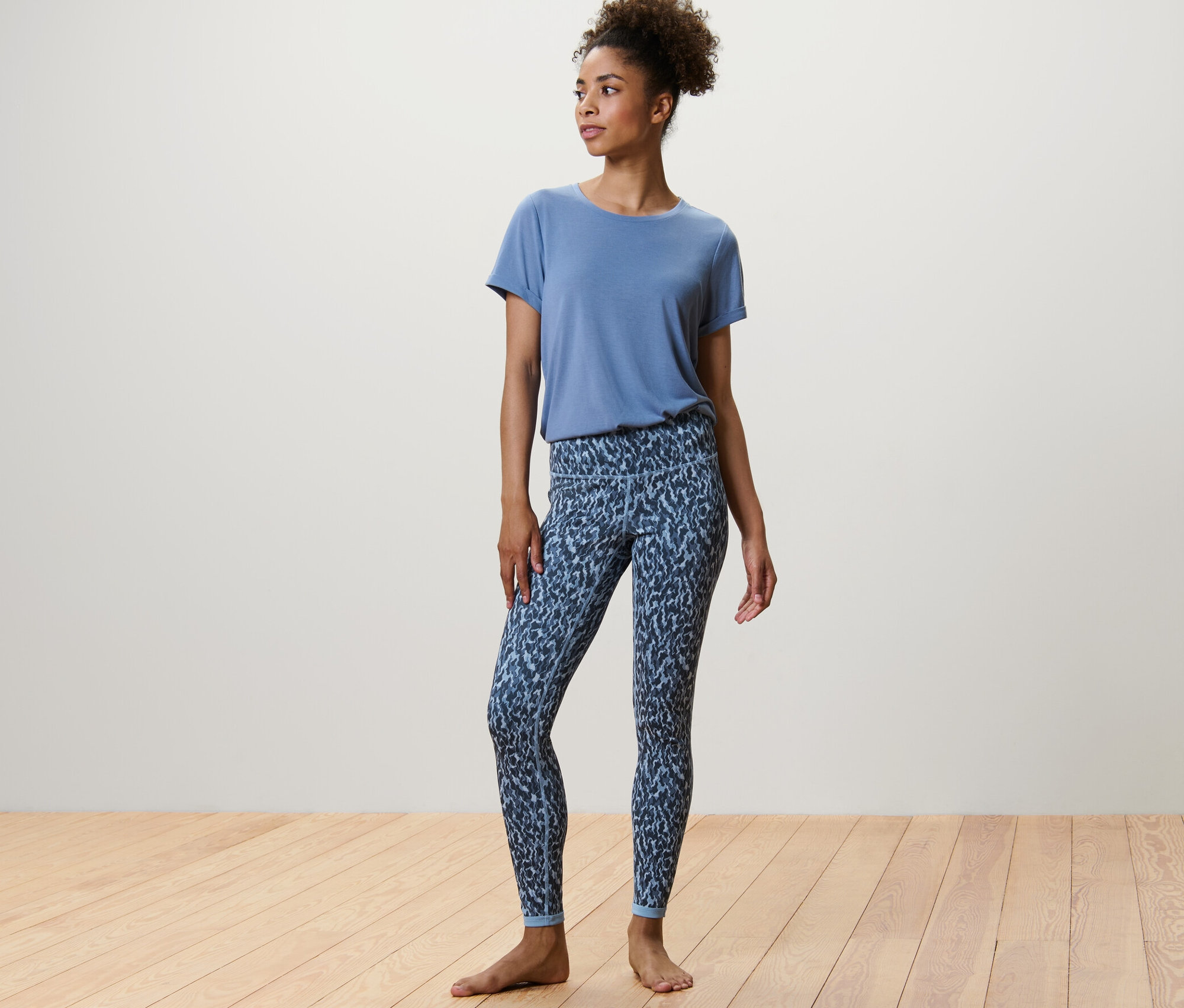 Une femme debout porte un legging de sport réversible bleu/bleu clair et un t-shirt bleu.