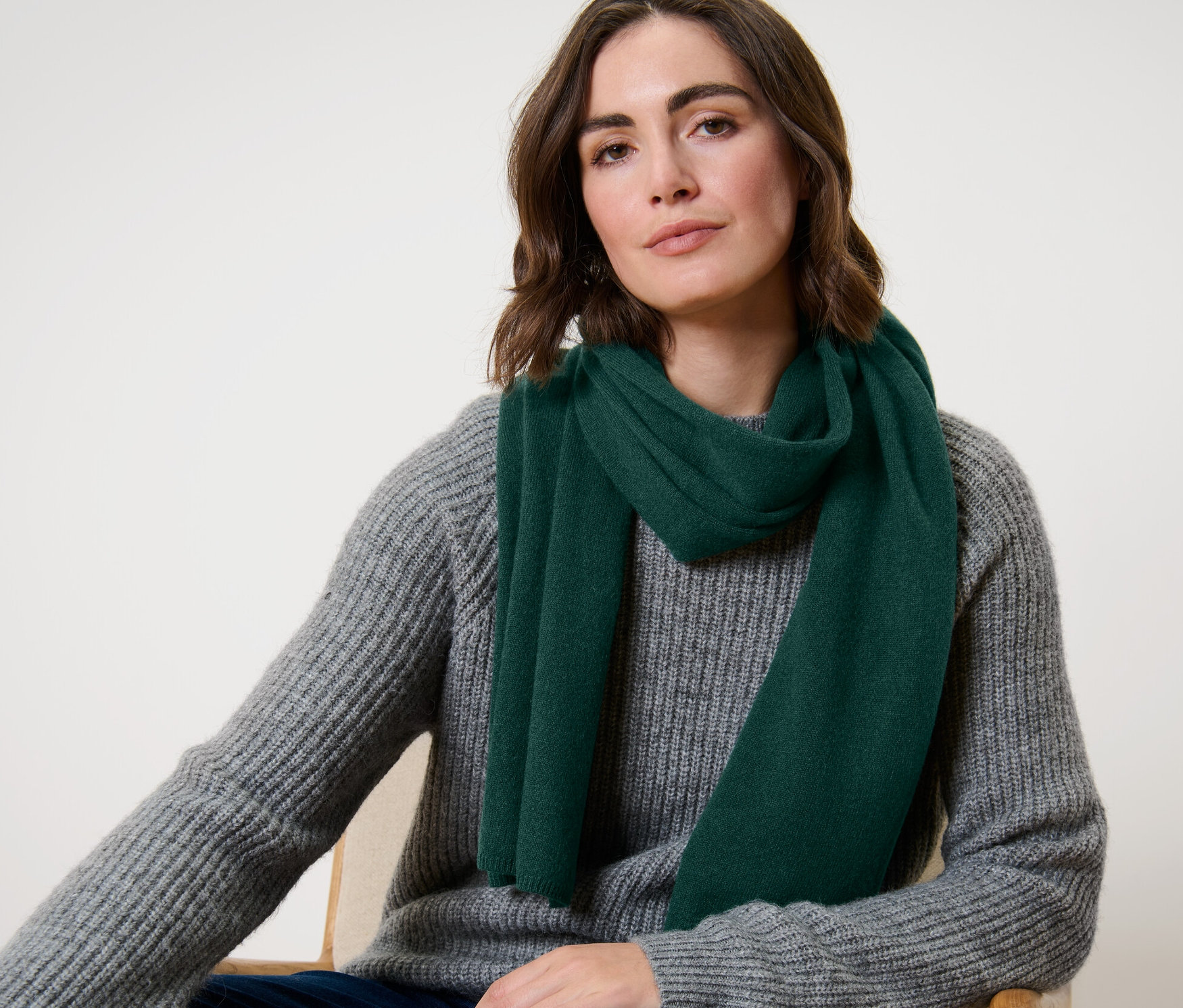 Femme assise portant une écharpe en cachemire tricoté vert foncé.
