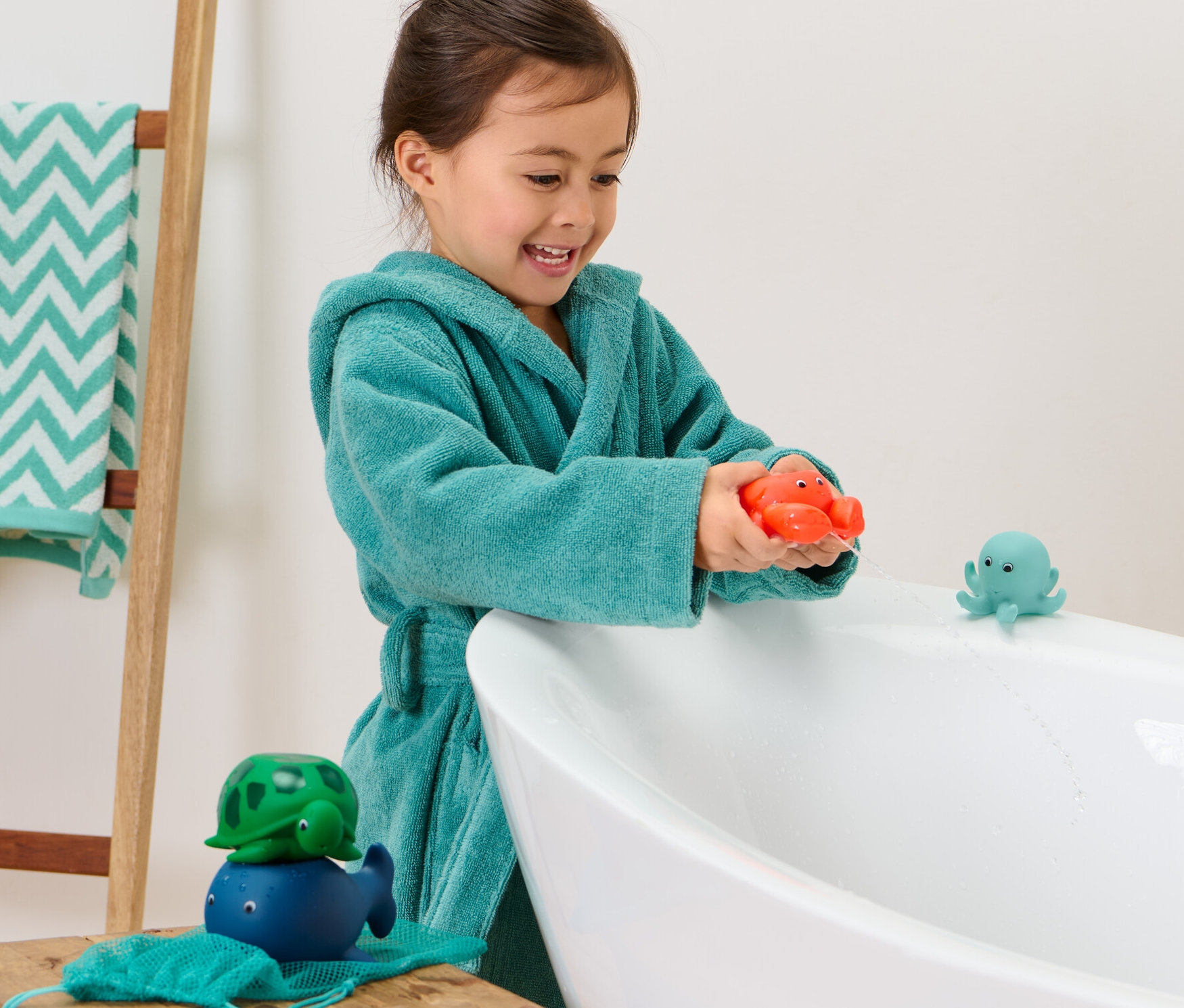 Une fille en peignoir joue avec 4 Animaux à jet d’eau dans la baignoire.