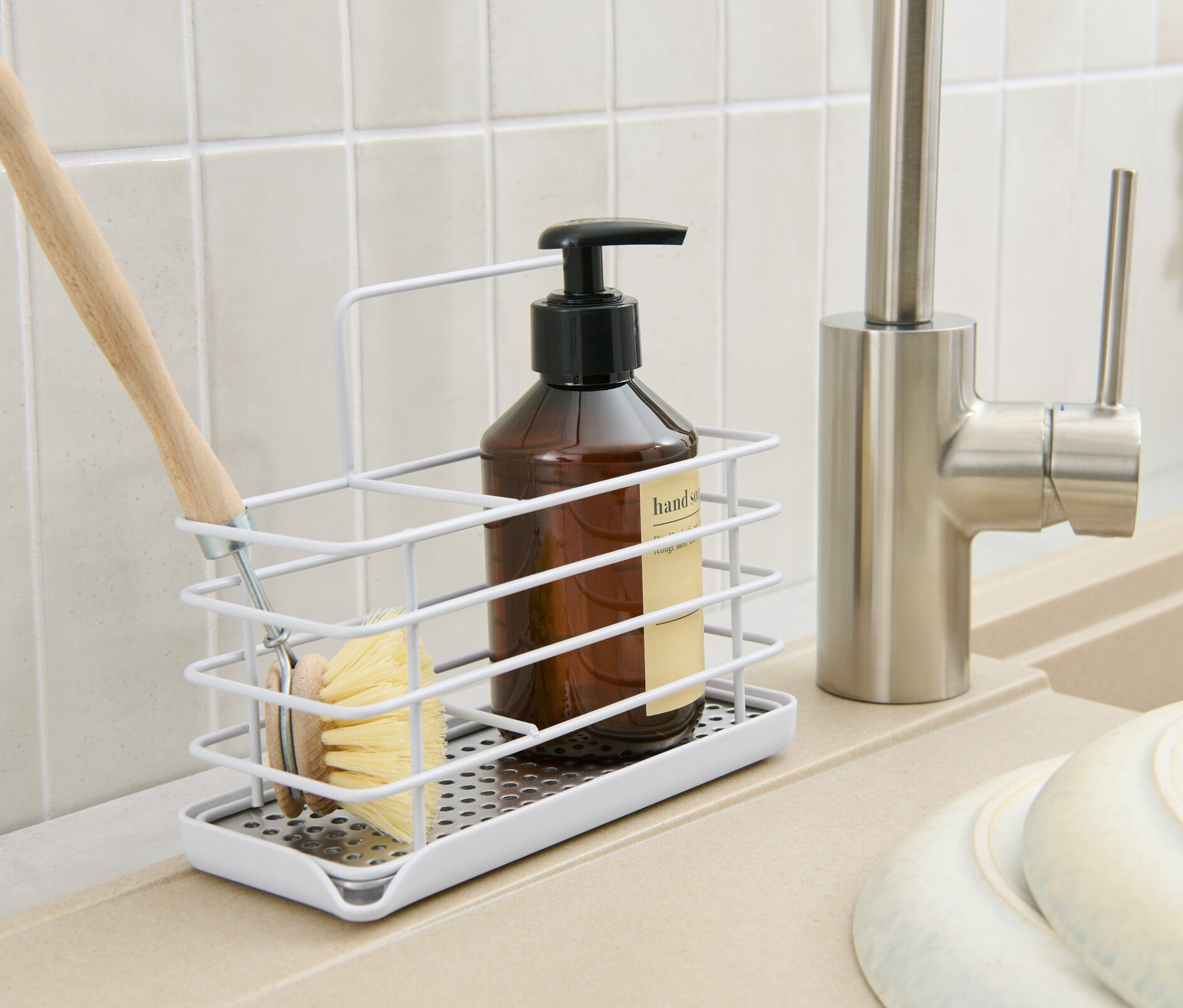 Dans une cuisine, un support en métal pour ustensiles de vaisselle avec une brosse, une bouteille et un distributeur de savon.