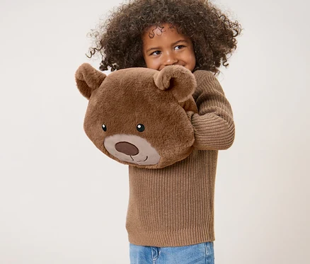 Fille aux cheveux bouclés tenant un coussin en peluche « ours ».