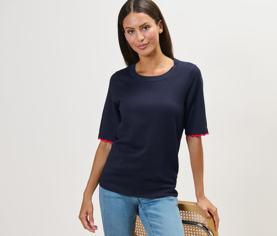 Une femme pose sur une chaise, portant un pull en maille fine bleu foncé et un jean.