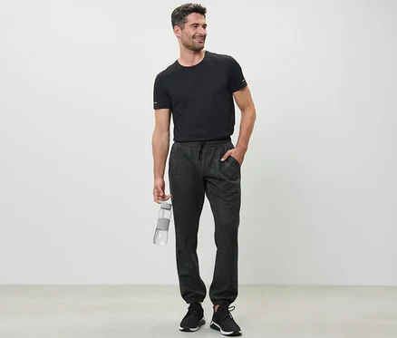 Un homme en t-shirt noir tenant une bouteille d'eau et portant un pantalon de survêtement.