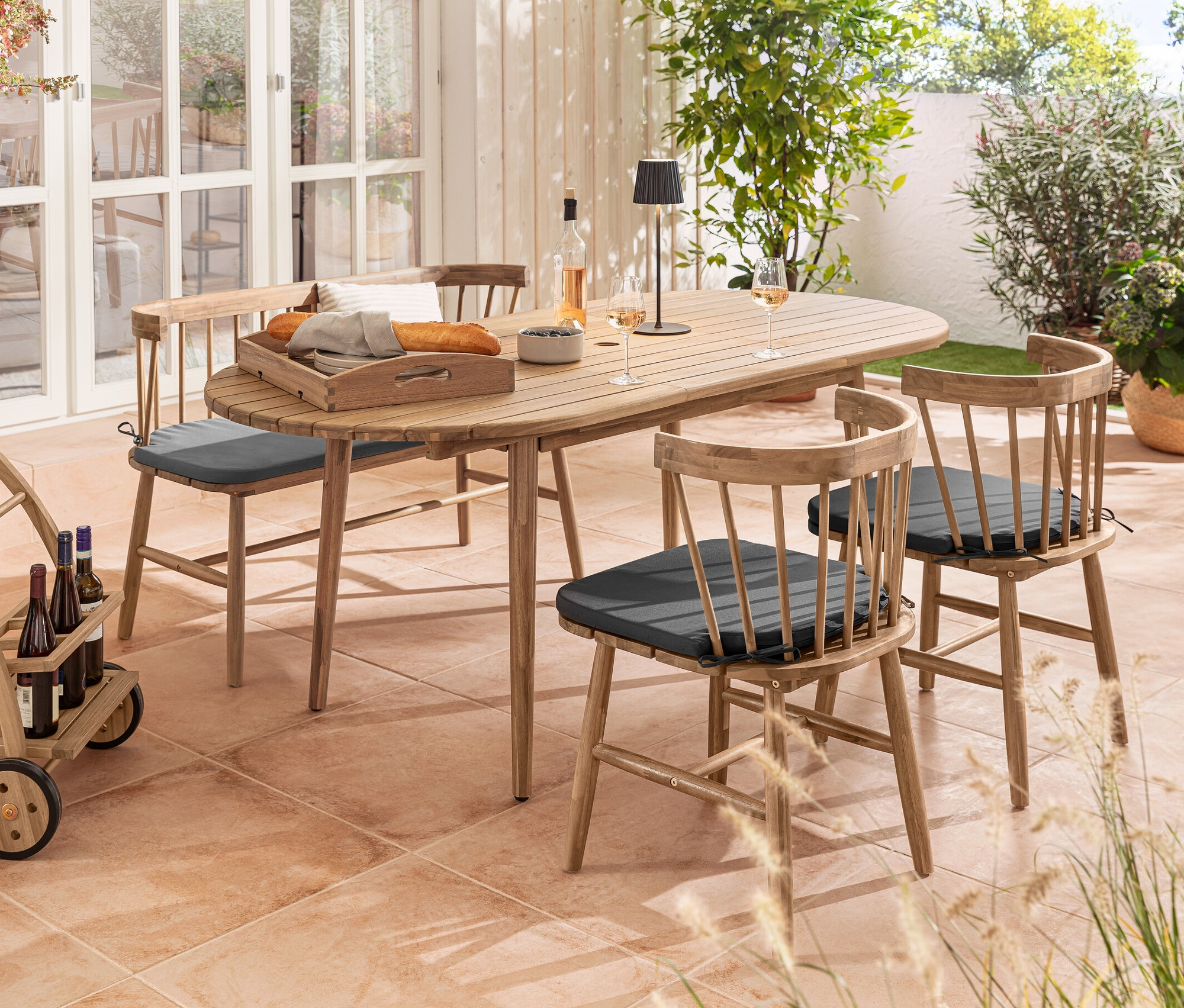 Extérieur avec table ovale extensible, chaises de salle à manger avec coussin d’assise, banc avec assise rembourrée et lampe de table d’extérieur à LED rechargeable noire.