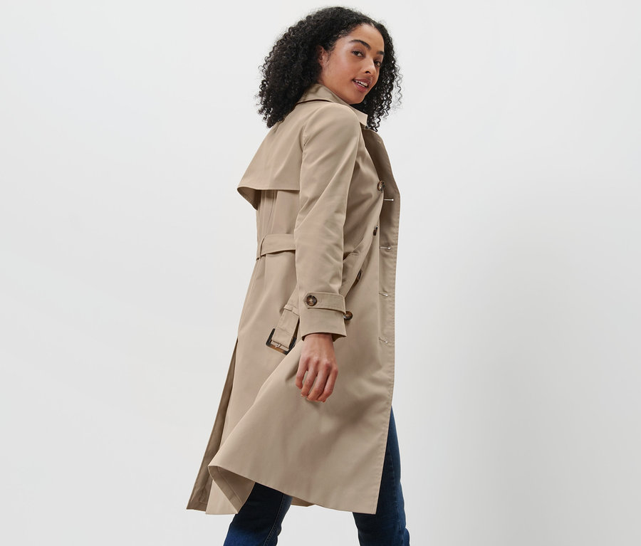 Une femme regarde par-dessus son épaule et porte un trench-coat beige.