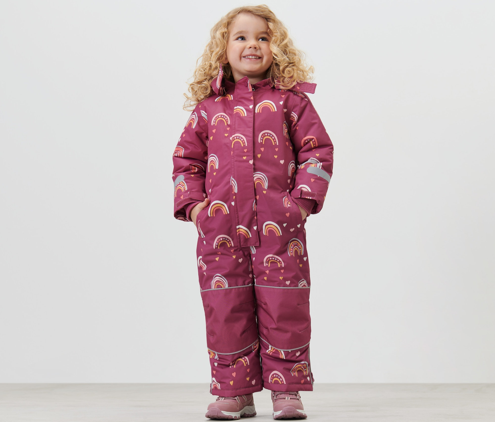 Fillette souriante posant en vêtements de neige pour enfant avec motif arc-en-ciel.