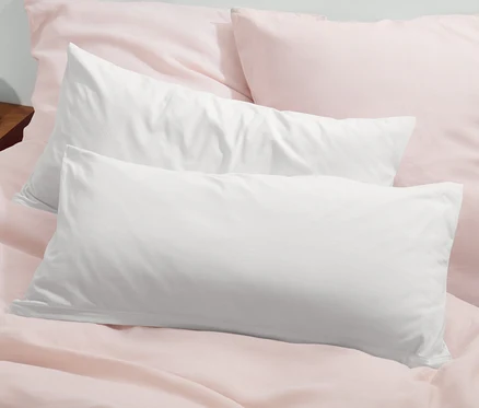 Deux taies d’oreiller en jersey blanc cassé sont posées sur un lit avec du linge de lit rose.