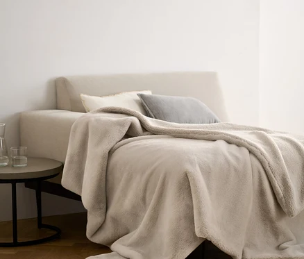 Une couverture moelleuse beige en fourrure synthétique est posée sur un lit avec des oreillers.
