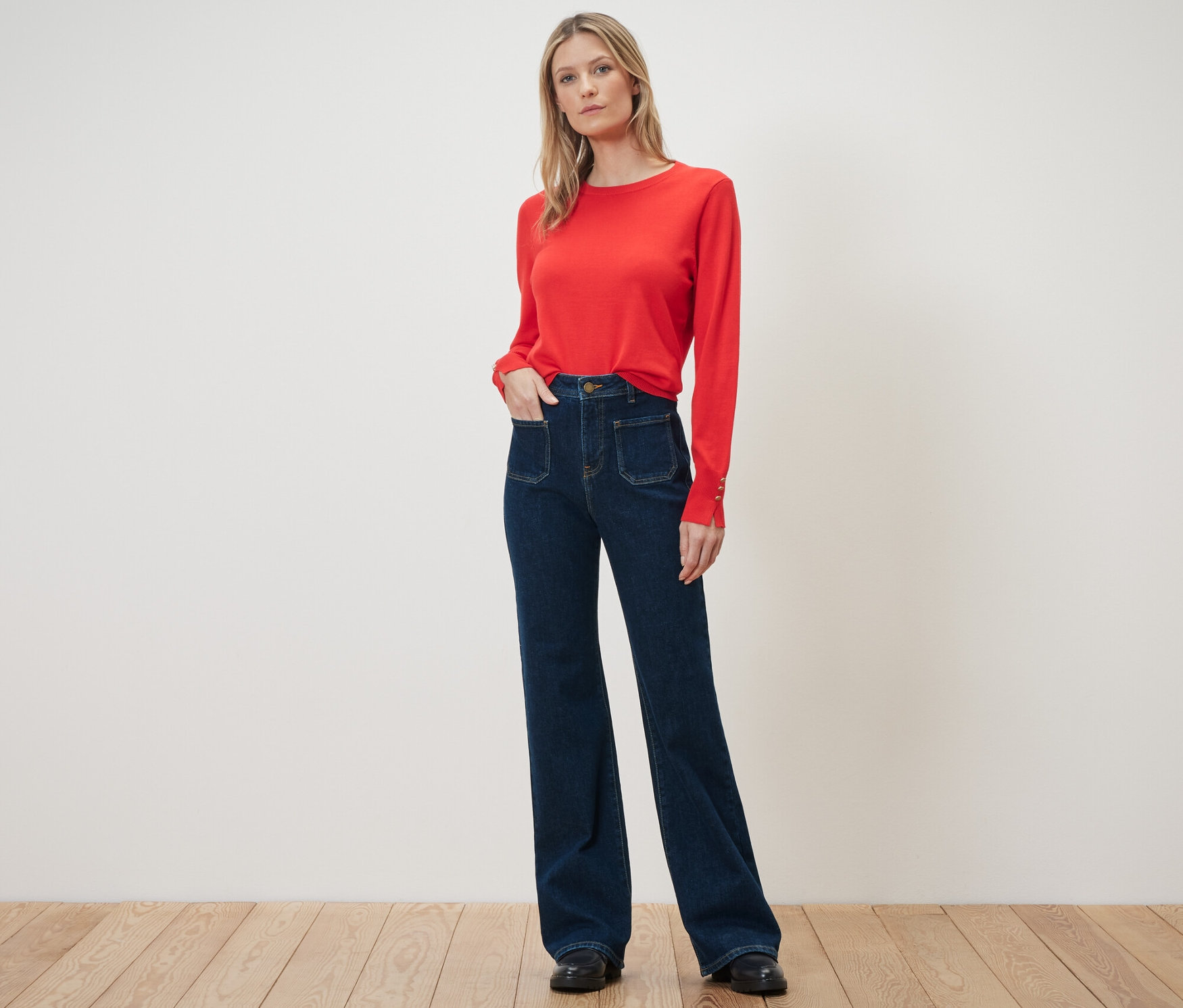 Une femme se tient debout et pose, portant un pull rouge et un jean évasé – Fit « Cara ».