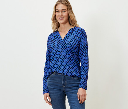 Une femme porte une blouse imprimée bleu cobalt et un jean.