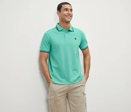 Un homme debout souriant portant un polo en piqué vert.
