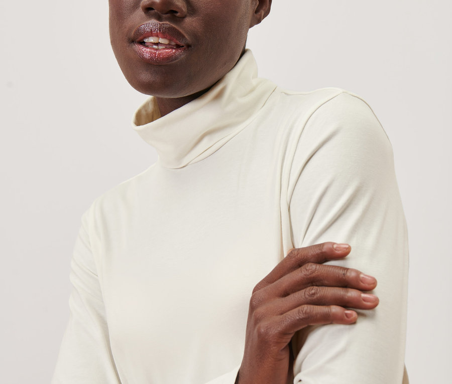 Une femme noire porte un t-shirt col roulé crème.