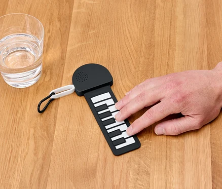 Une main joue sur un mini-piano à côté d'un verre d'eau.