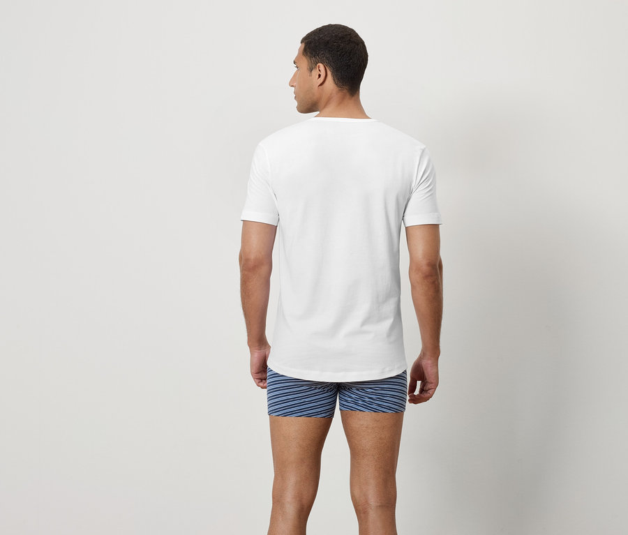 Un homme dos à la caméra portant un t-shirt blanc et un caleçon rayé bleu.