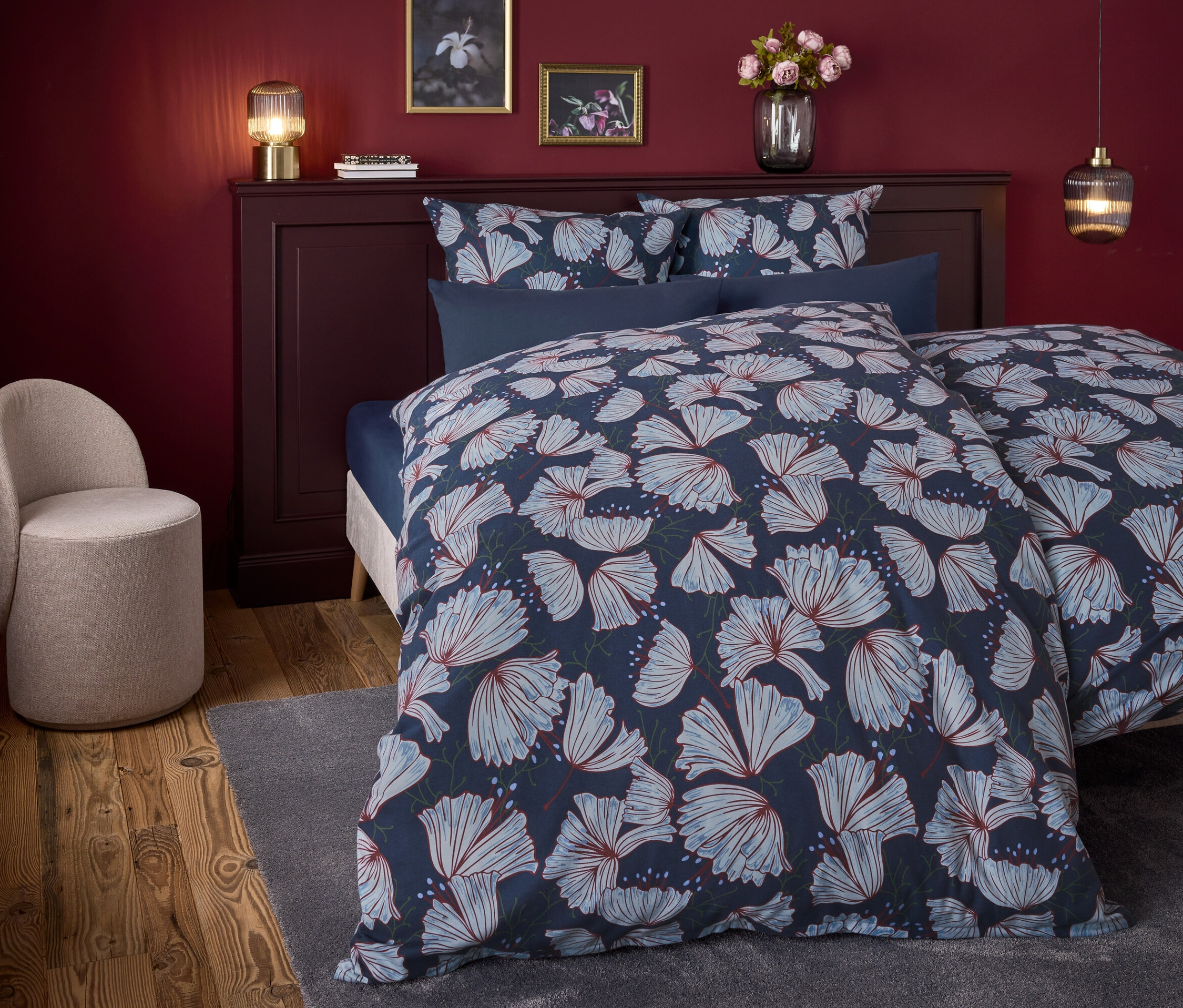 Chambre avec un lit avec des draps à fleurs bleues et un fauteuil beige.