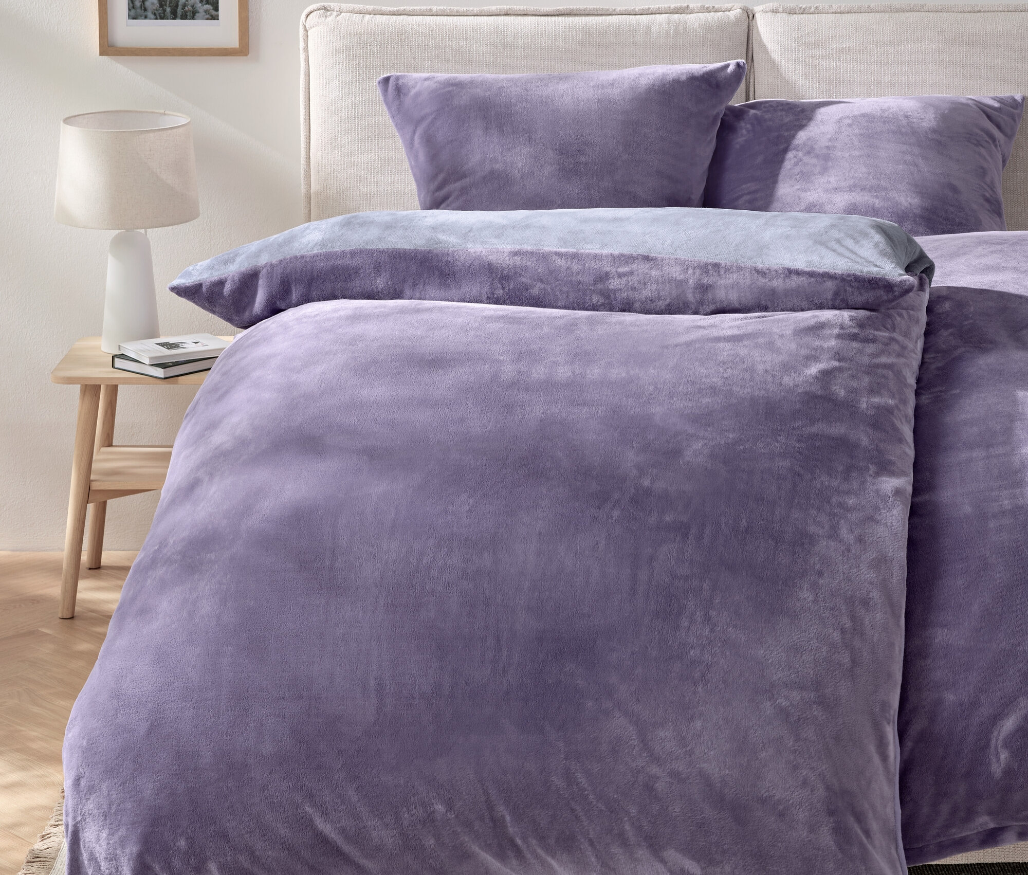 Linge de lit violet sur un lit avec deux oreillers et une table de chevet avec une lampe.