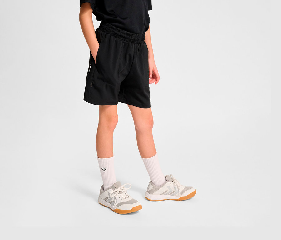 Un garçon porte un short d'entraînement HUMMEL HMLJR Pulse noir et des baskets.