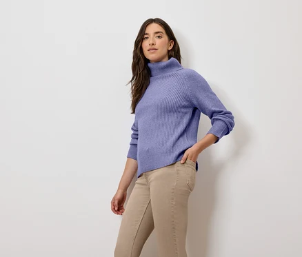 Femme posant en pull à col roulé lilas et pantalon beige.