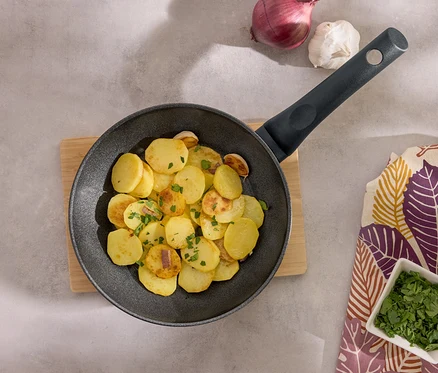 Pommes de terre sautées dans une poêle noire sur une planche à découper en bois avec de l'ail, des oignons et du persil.