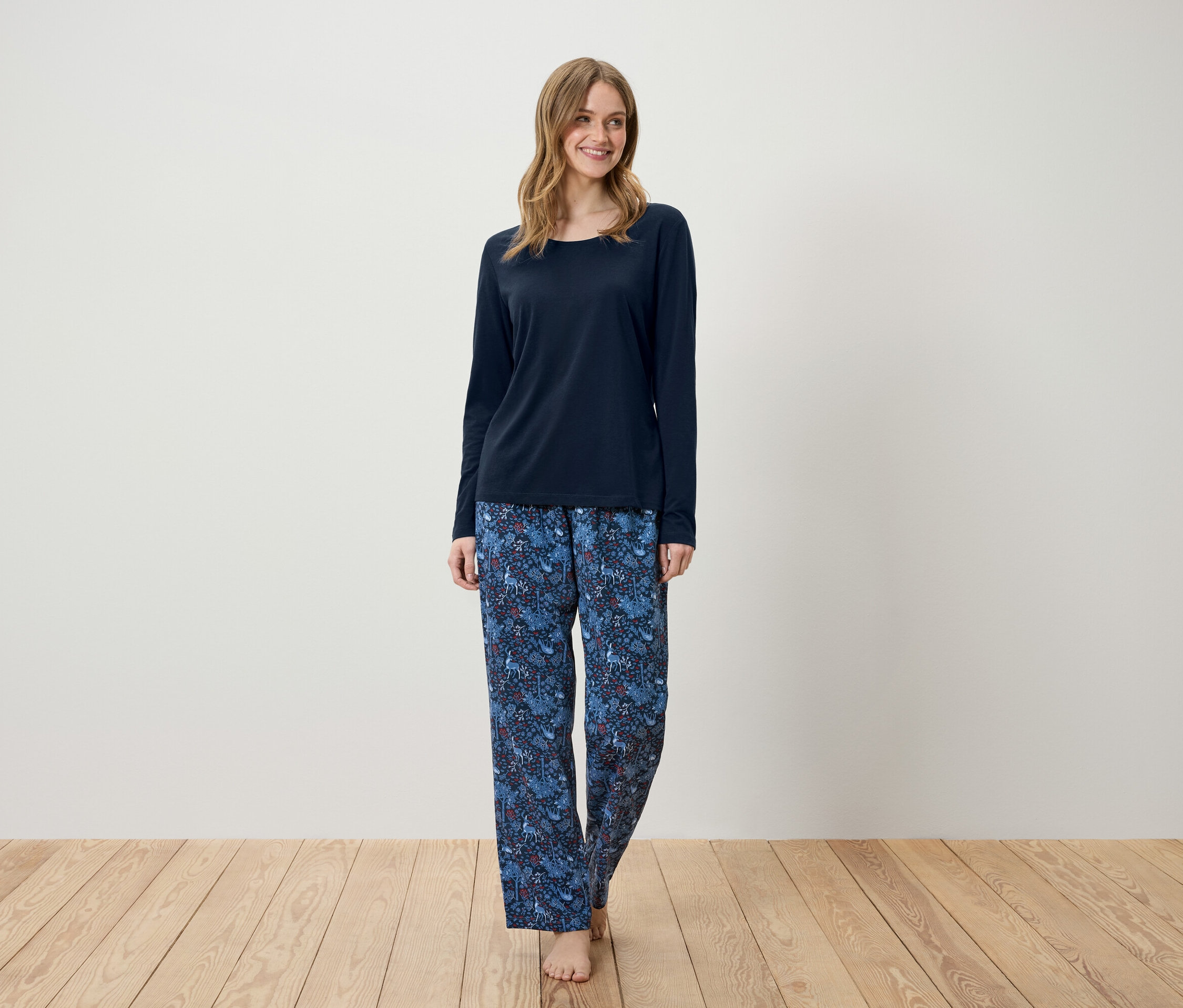 Une femme debout portant un pyjama bleu marine à manches longues et un pantalon bleu à motifs.