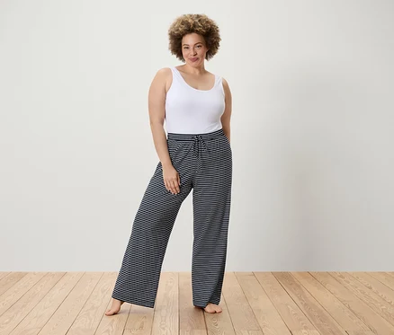 Femme posant en débardeur blanc et pantalon rayé.