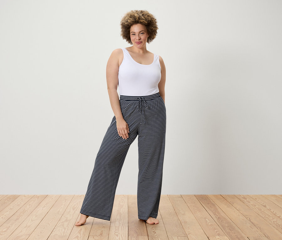 Femme posant en débardeur blanc et pantalon rayé.