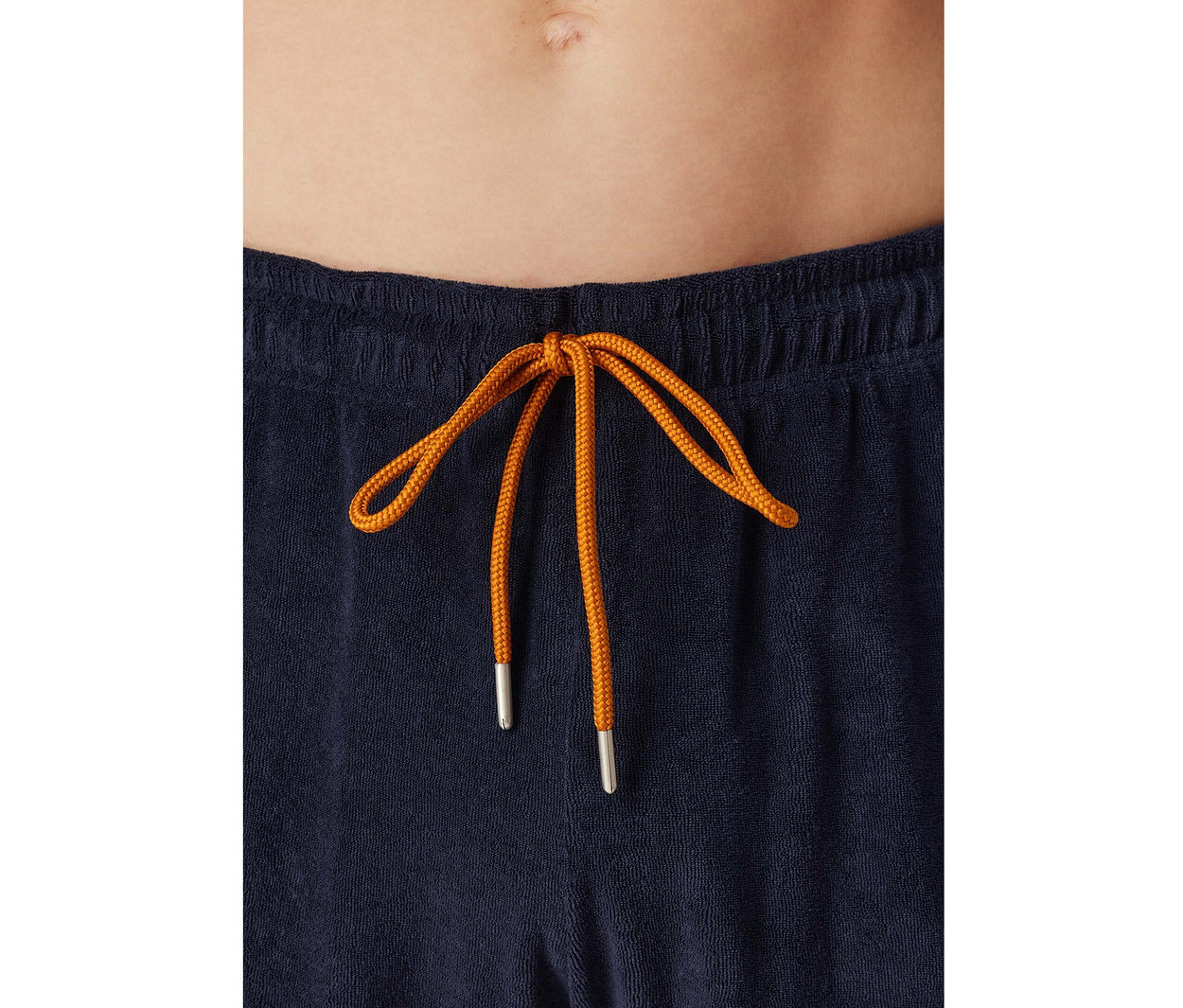 Gros plan sur le ventre d'une personne portant un bas de pyjama SCHIESSER en tissu éponge bleu marine avec un cordon orange noué.