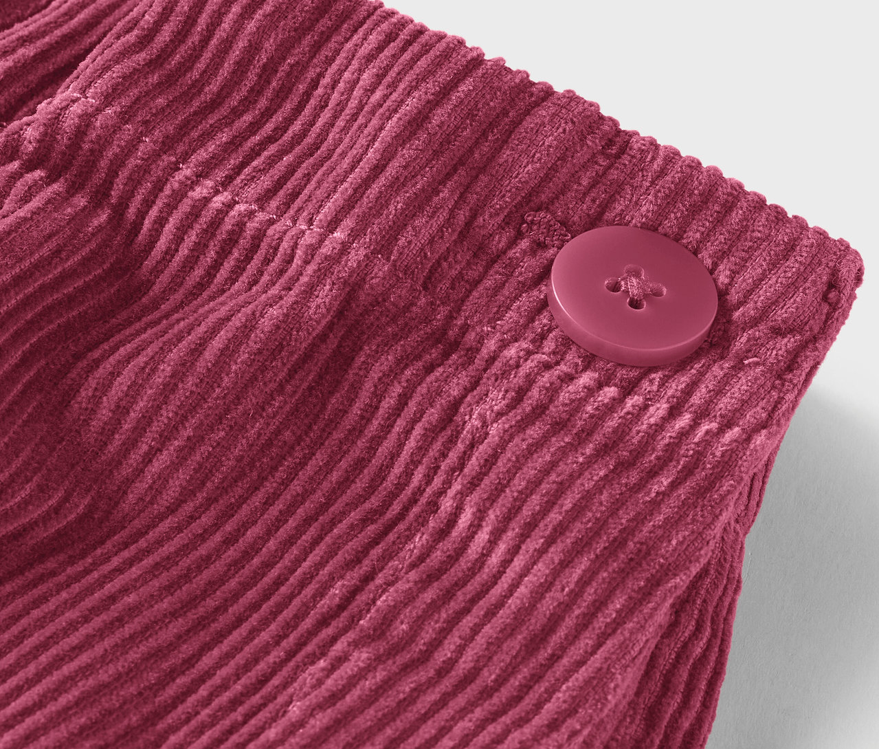 Gros plan d'un tissu de velours côtelé bordeaux avec un bouton.