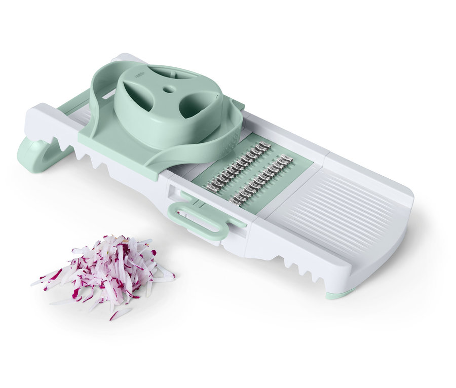 Une mandoline blanche avec des accents vert clair à côté d'oignon rouge coupé.