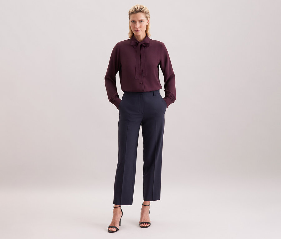 Femme portant un chemisier à col lavallière en viscose Seidensticker bordeaux, un pantalon foncé et des sandales noires.